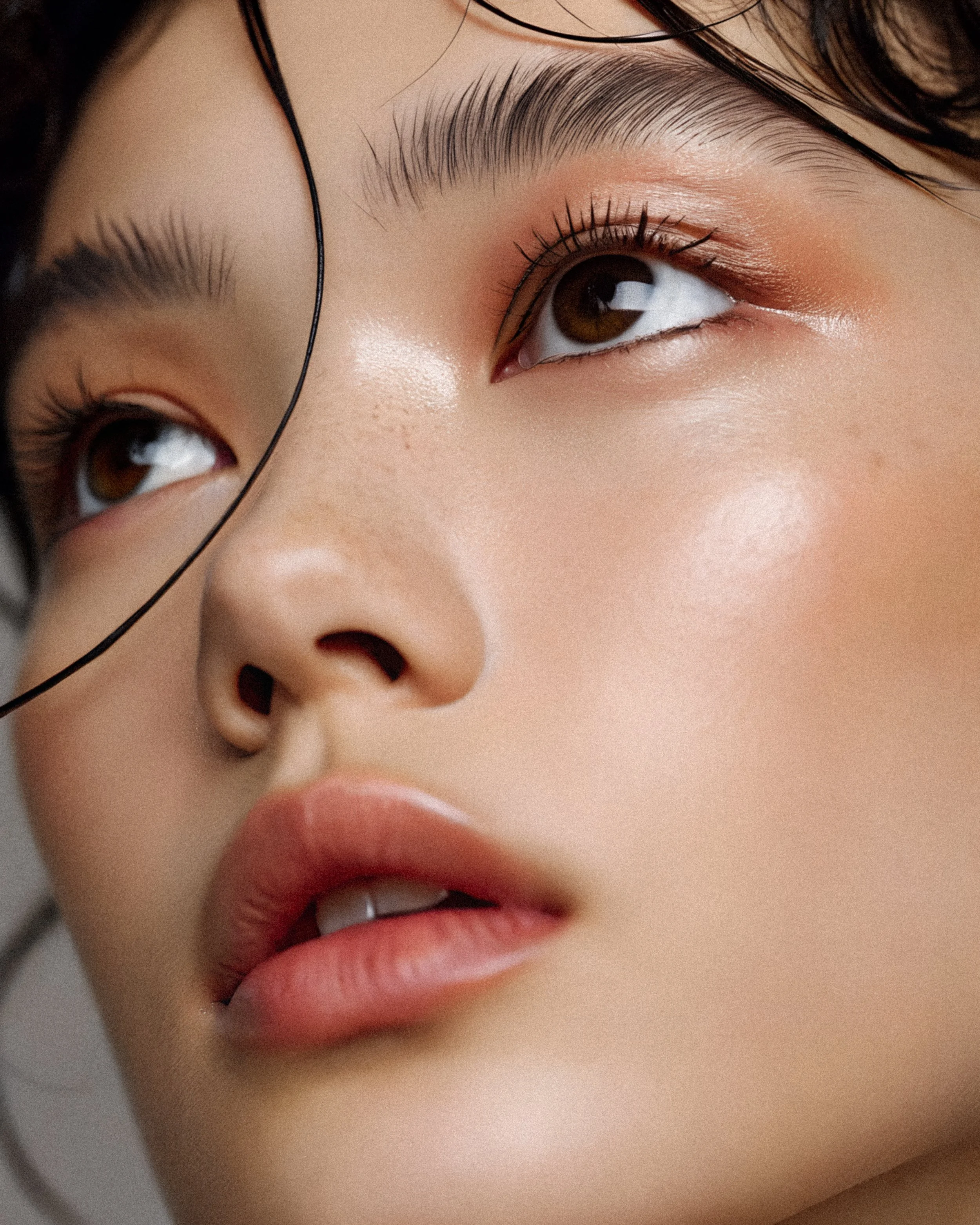 Close-up of a woman's face showing her eye, eyebrow, part of her nose, and lips, with professional makeup and soft lighting.