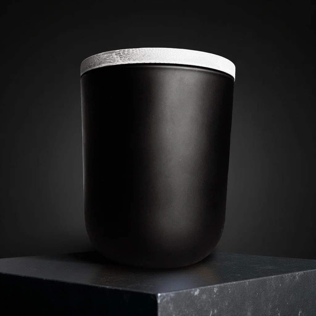 A black, matte insulated tumbler candle jar with a wood lid on a dark surface against a black background.