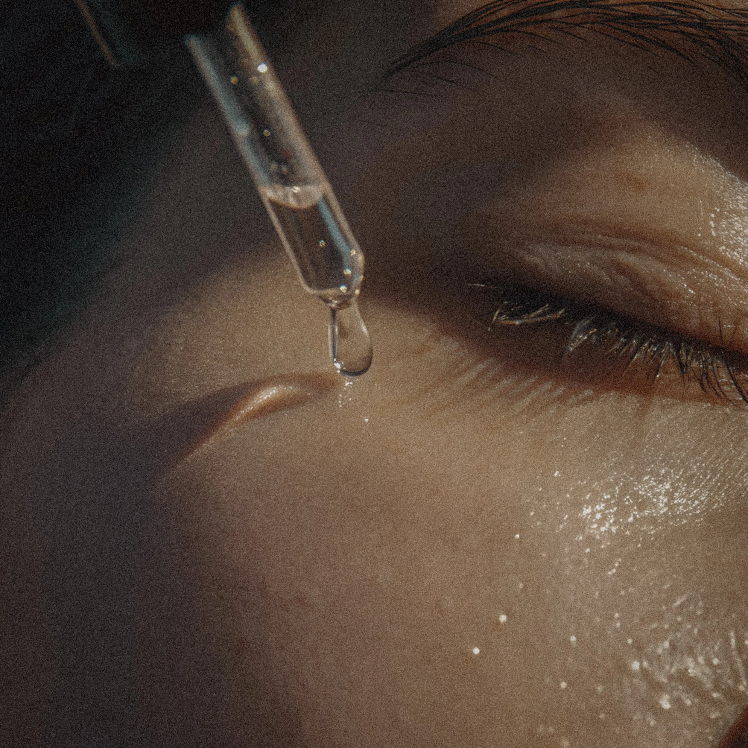 Close-up of a person's face with a dropper above the skin, likely applying facial serum or oil.