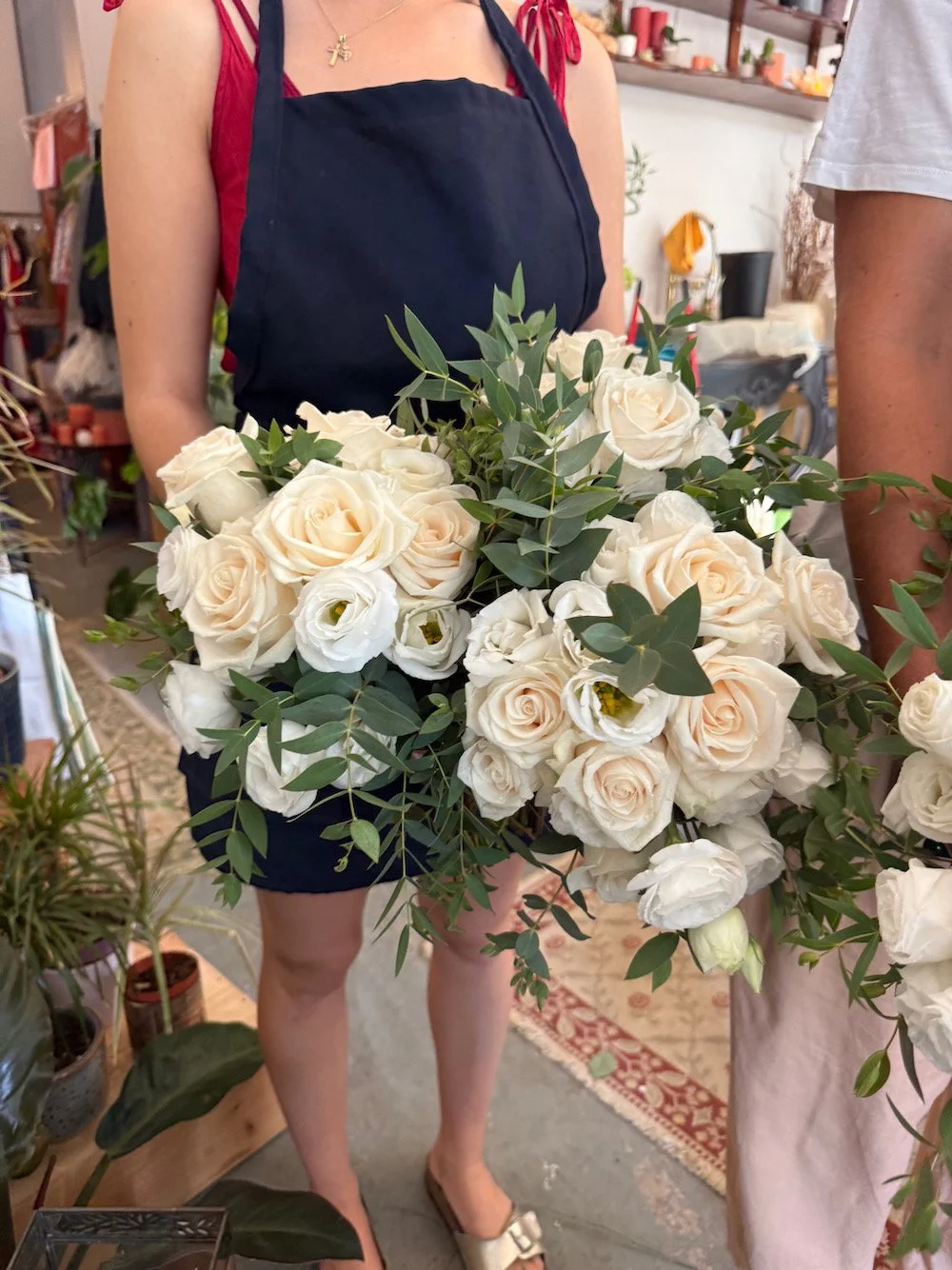 Person holding a large bouquet of white roses and greenery in a flower shop.