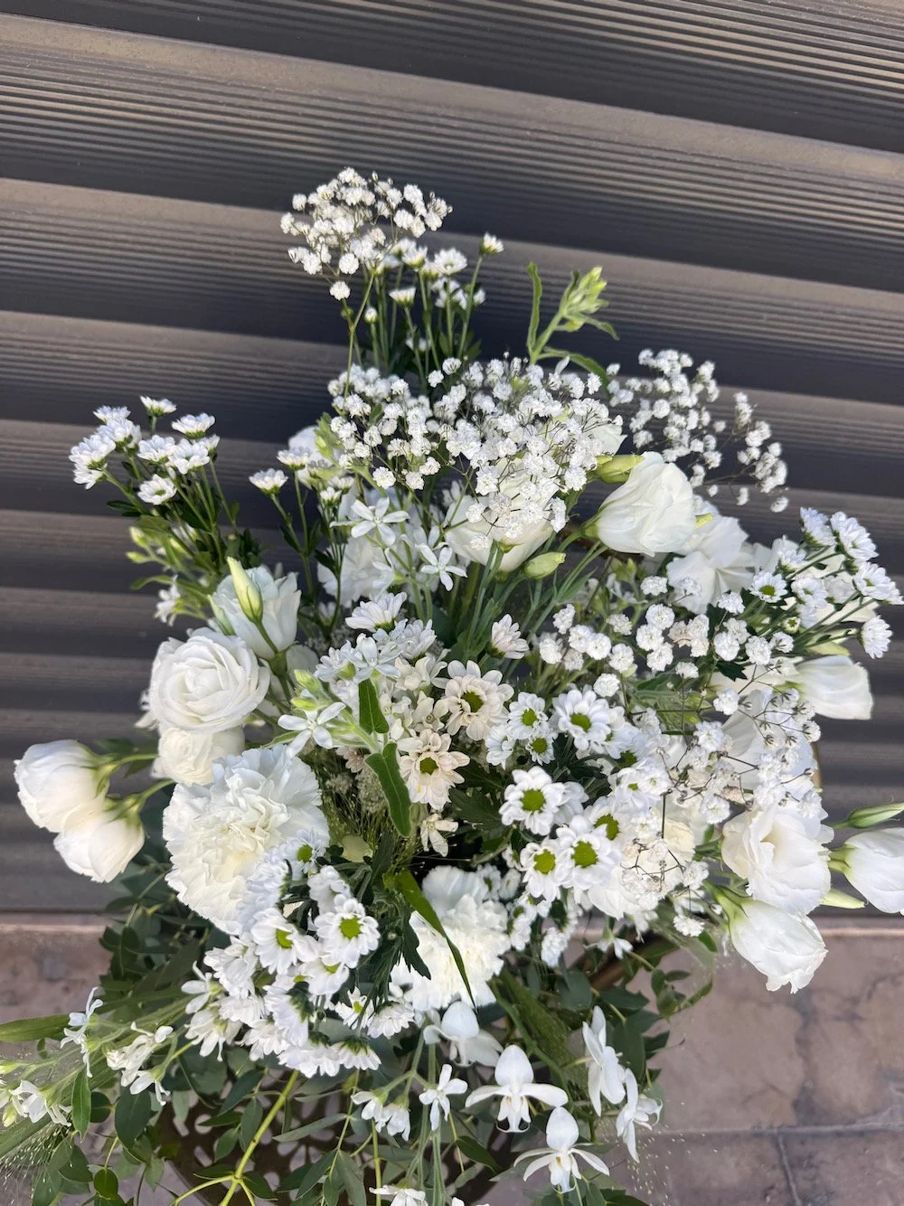 A bouquet of white flowers including ranunculus, daisies, and baby's breath, set against a gray textured background.