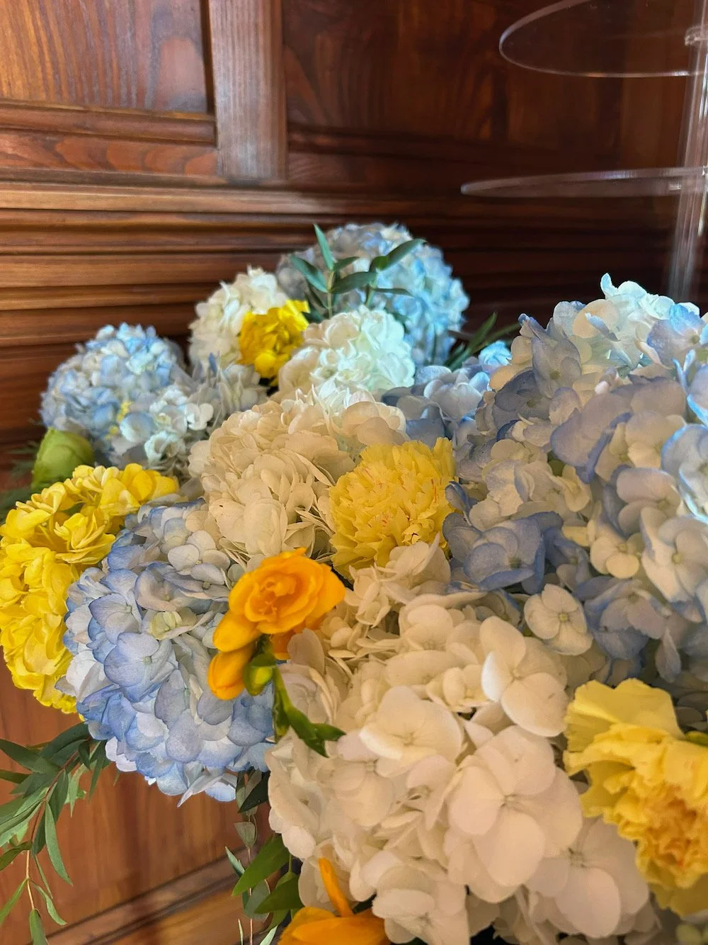 A bouquet of blue, white, yellow, and orange flowers against a wooden background.