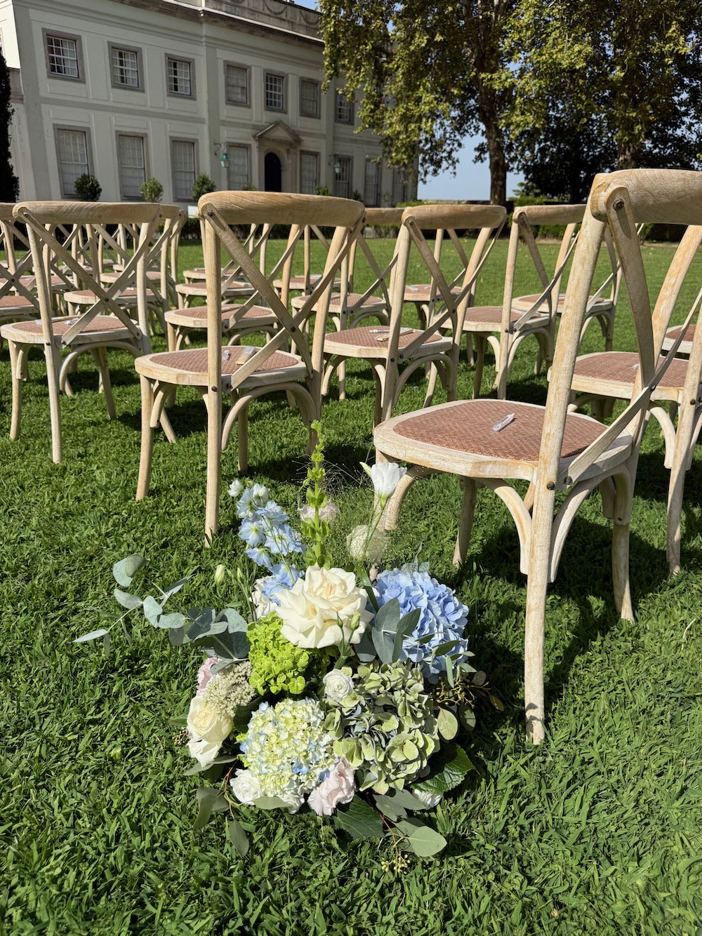 Chairs arranged outdoors on green grass with a floral bouquet in the foreground and a large historic building in the background.