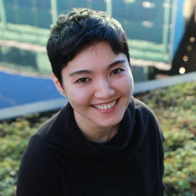 Close-up of a smiling woman with short black hair outdoors.