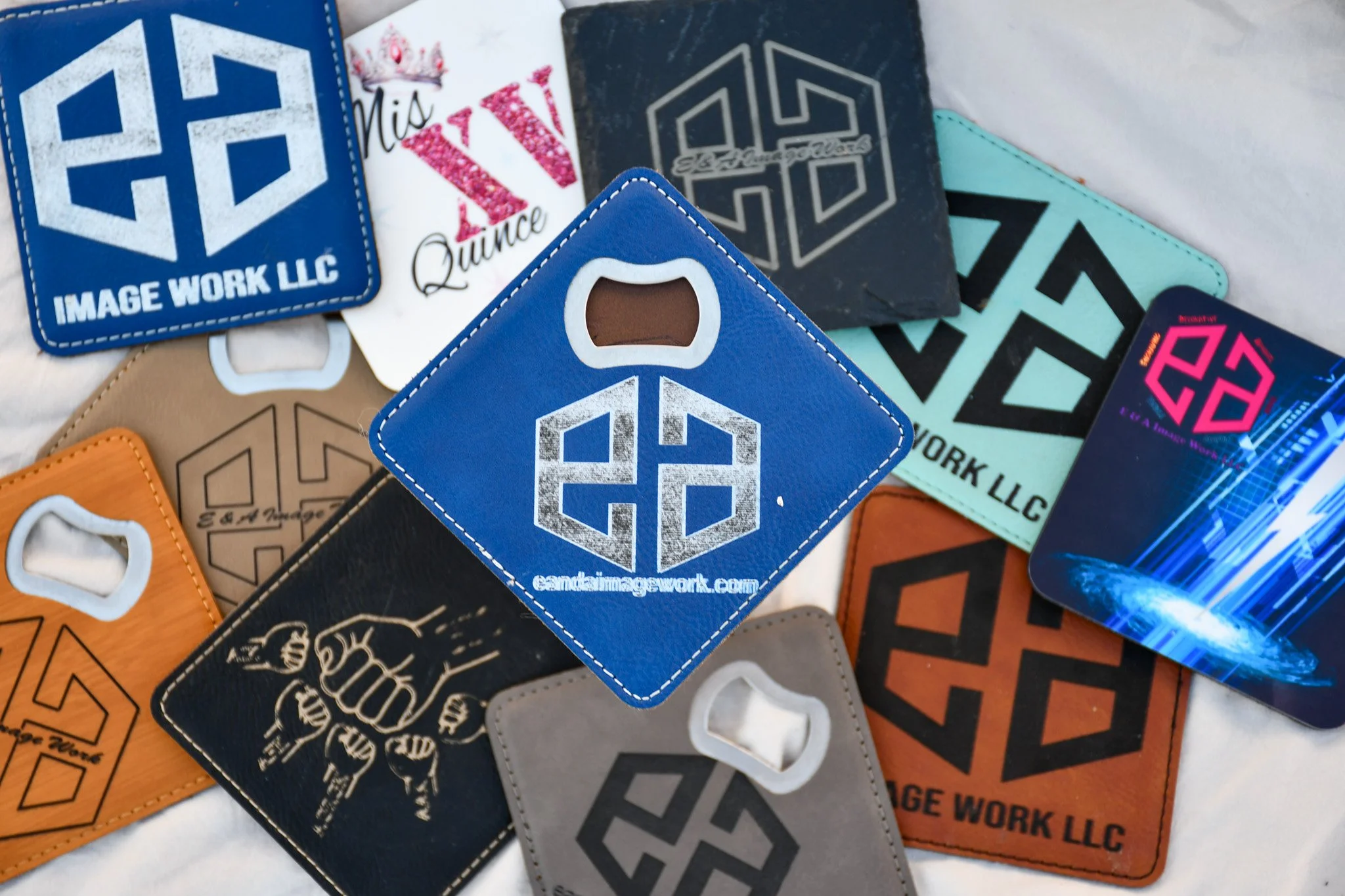 A collection of square and diamond-shaped leather patches with various logos, designs, and website URLs, some featuring fist and animal imagery, in colors including blue, black, tan, gray, orange, and multicolor, scattered on a white surface.
