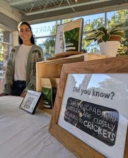 A woman is smiling at Fulton Street Farmer's Market next to a table with The Green Leap product.