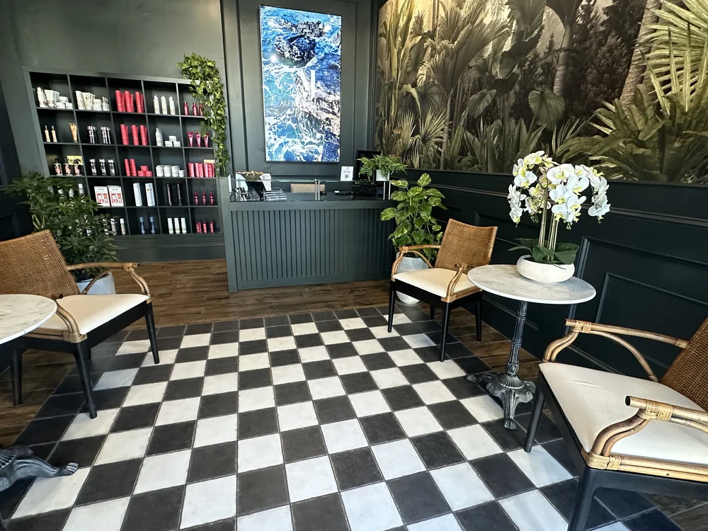 La sala de espera de Alfredo James Hair Design en San Antonio, con piso a cuadros, sillas de ratán y una pared iluminada de productos