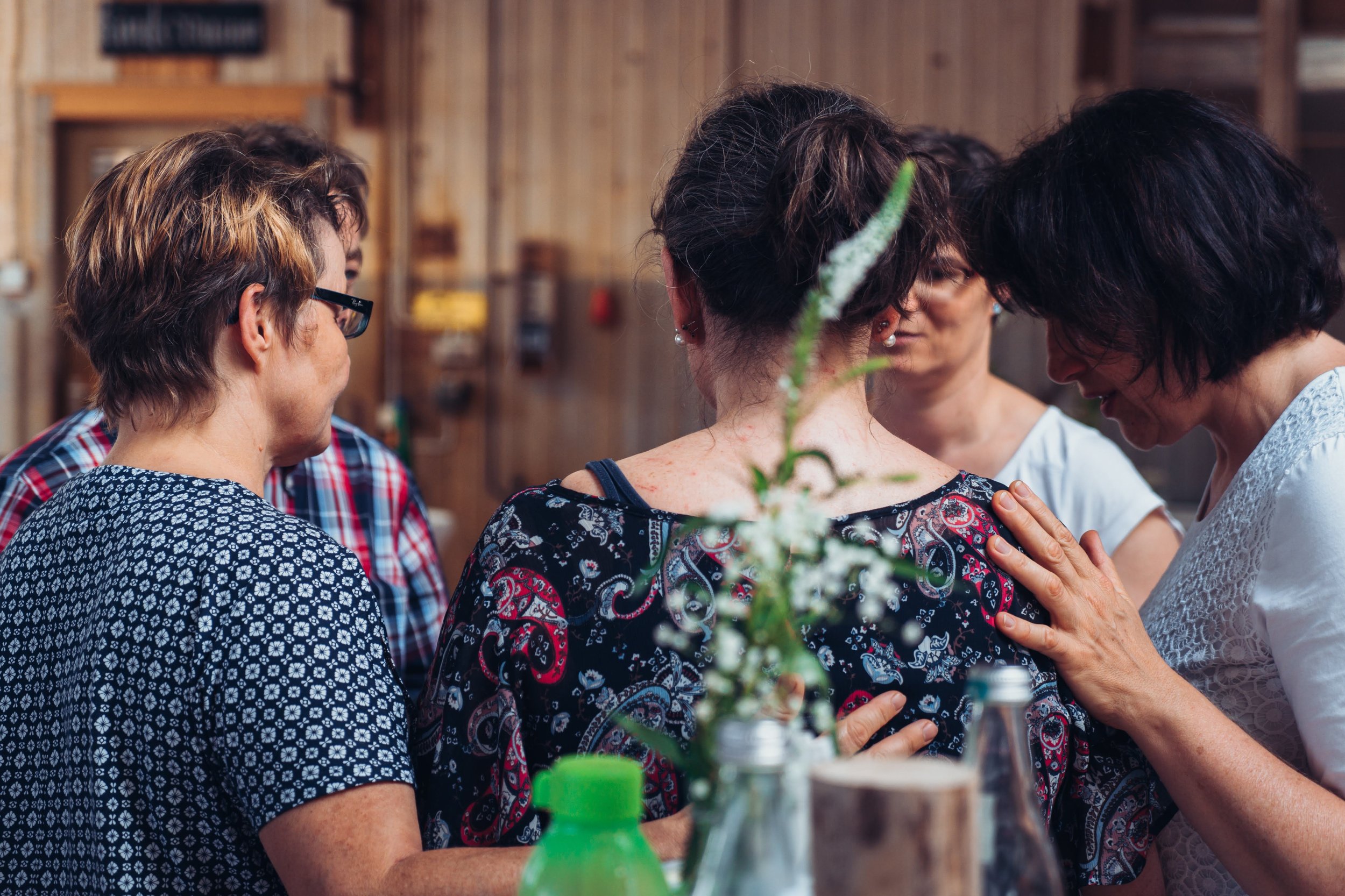 Gruppe von Frauen, die sich umarmen und gegenseitig berühren, in einer rustikalen, holzverkleideten Umgebung.