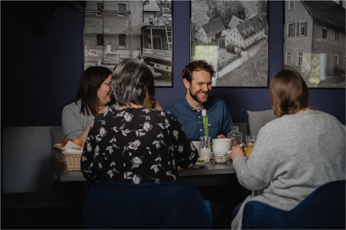 Fünf Menschen sitzen sich an einem Tisch im Restaurant gegenüber und lachen, während sie Getränke trinken und eine Vase mit Tulpen hat.