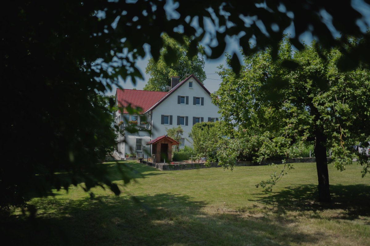 Ein Haus mit rotem Dach, umgeben von Bäumen und einem grünen Garten, fotografiert an einem sonnigen Tag.