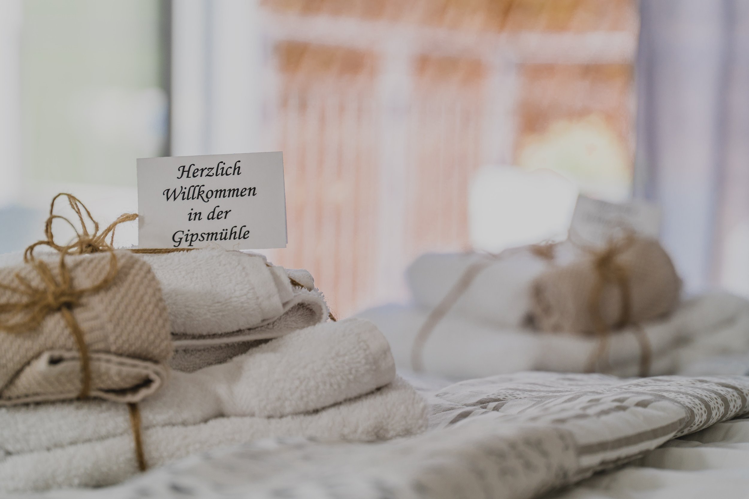 Weiß handtücher und Stoffbündel auf einem Tisch, mit einem Begrüßungsschild «Herzlich Willkommen in der Gipsmühle»