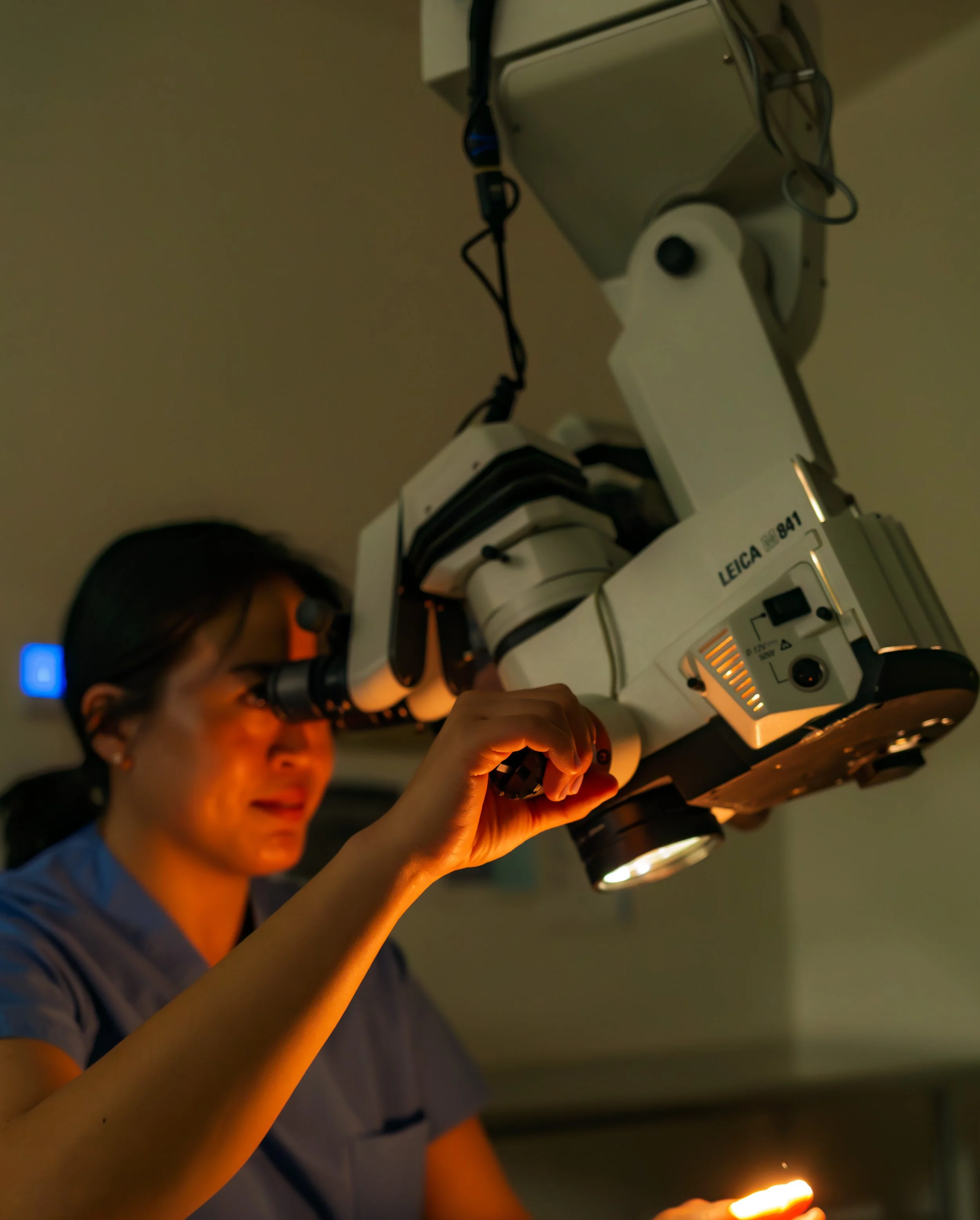 A doctor standing in a medical room with advanced medical equipment, including a microscope, computer, and examination table.