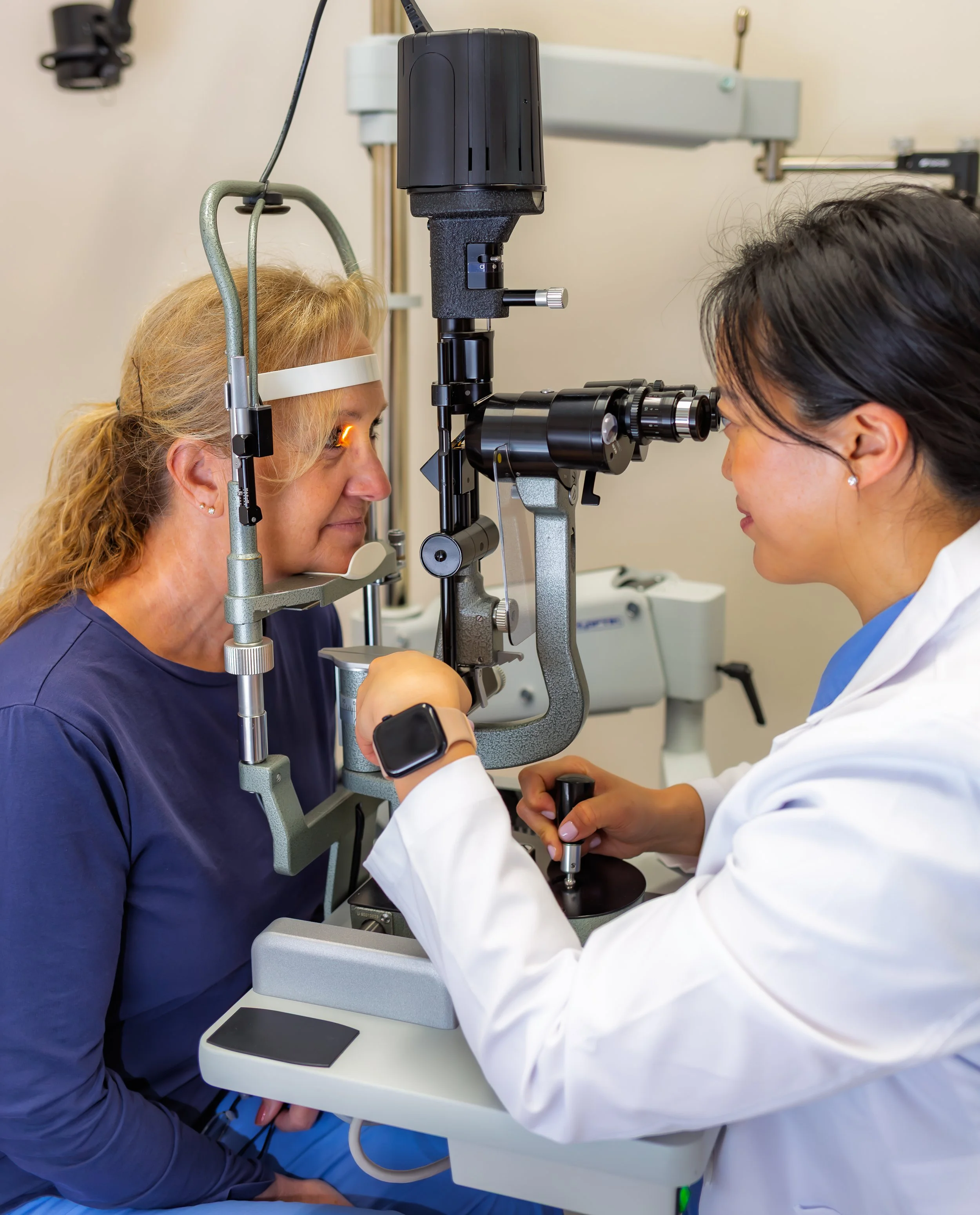 Optometrist assisting a patient during an eye exam using a specialized eye testing machine in an optometry clinic.