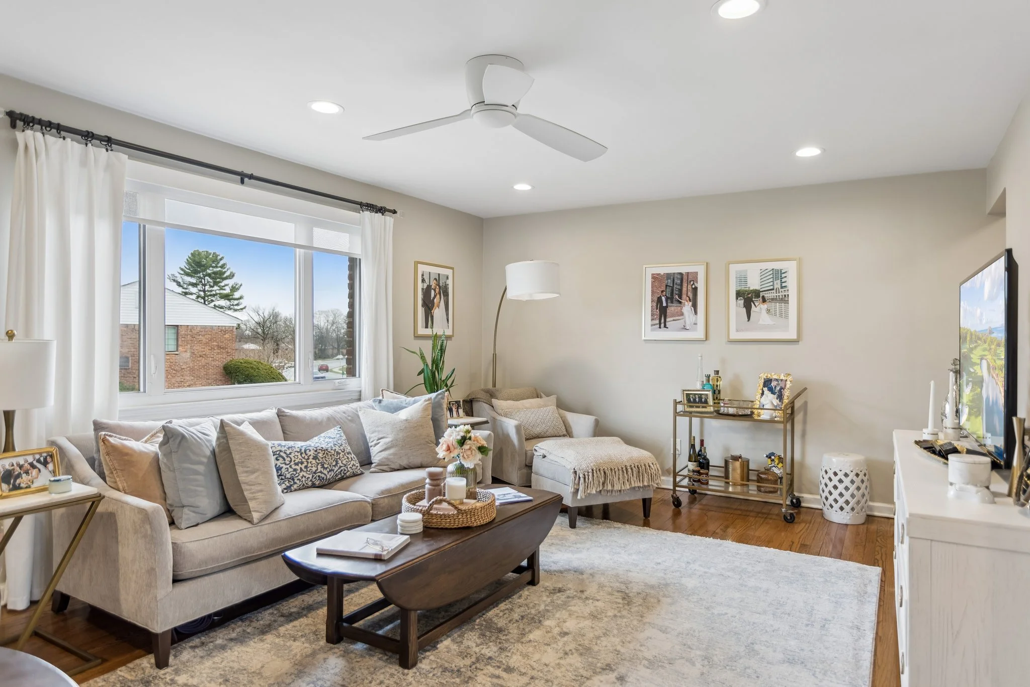 Living room with beige sofa, coffee table, wall art, and large window with white curtains