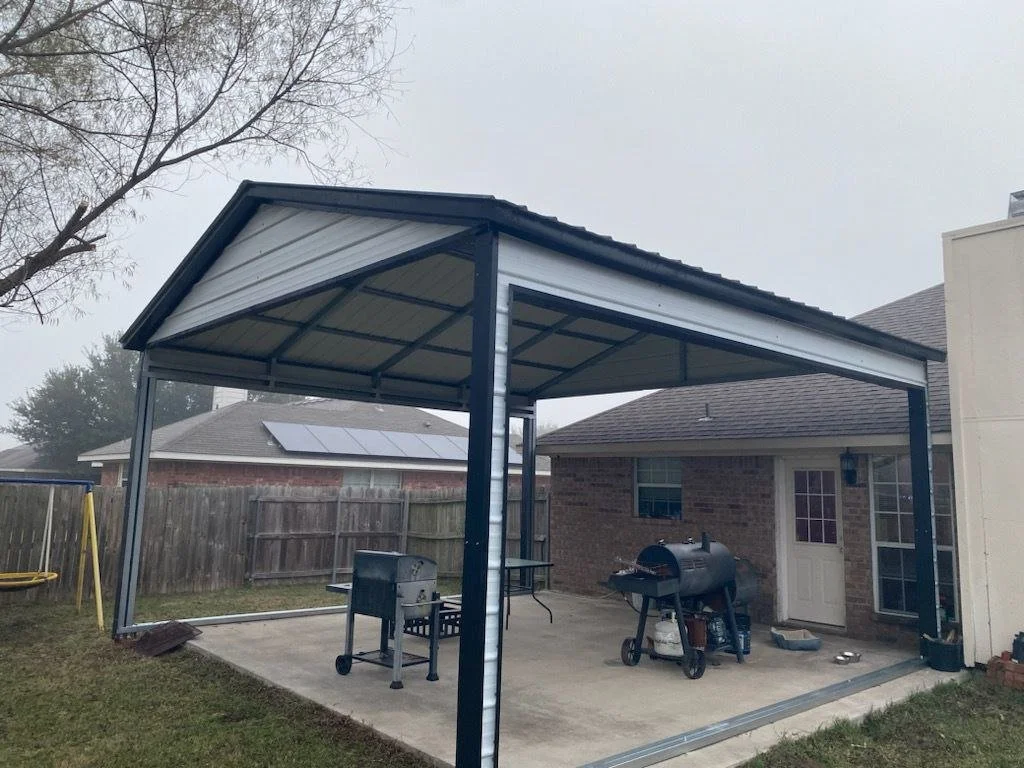 A backyard covered patio area with a metal roof, a brick house with a door and window, a barbecue grill, and a child’s yellow swing set.