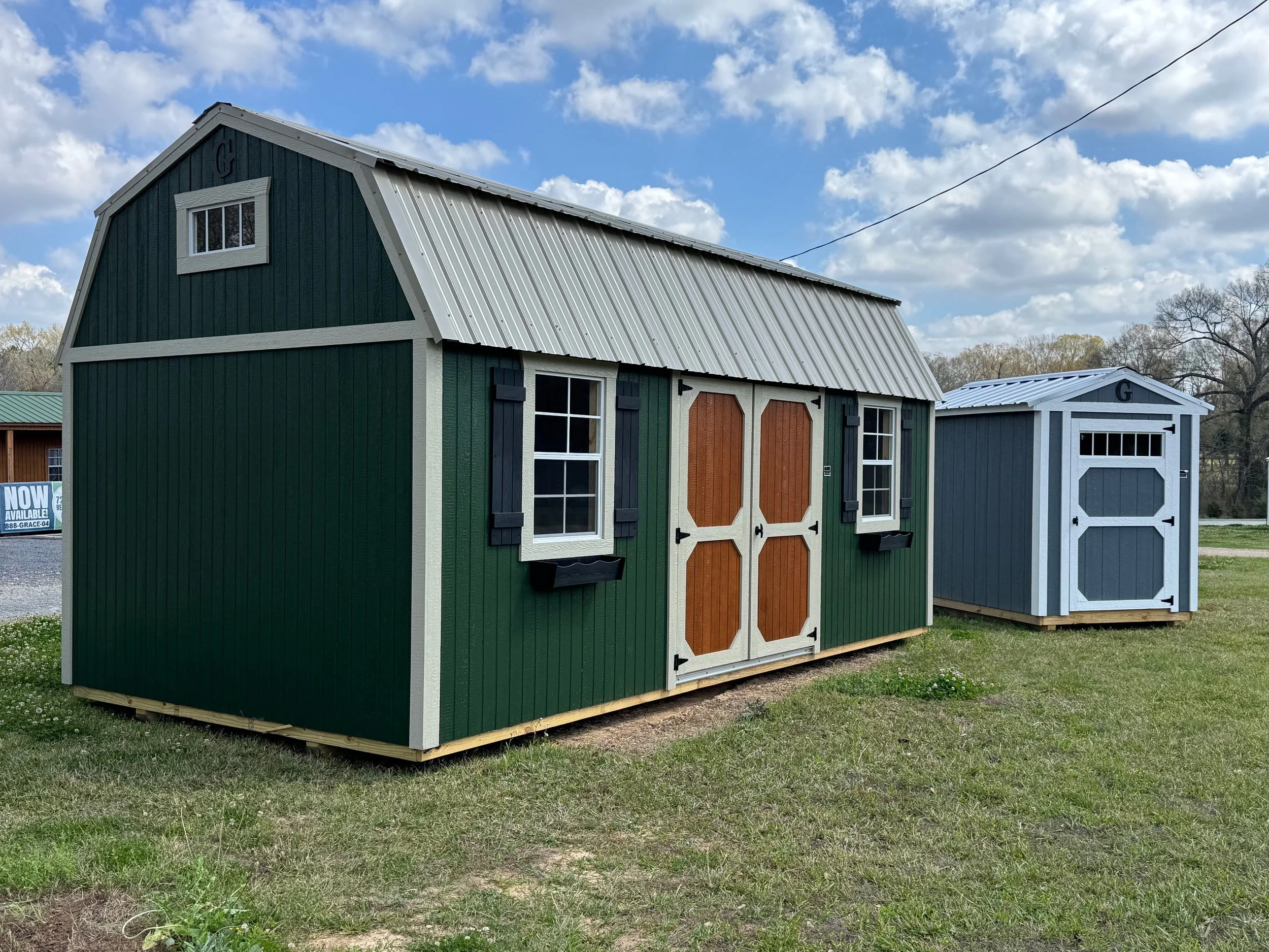 A 10'x20' Graceland Portable Building in a Side Lofted Barn model with transom windows, 2'x3' Windows with shutters and flowerboxes, a Double Wood Door with the optional stained door, and is finished in pine green with light khaki trim and metal roof