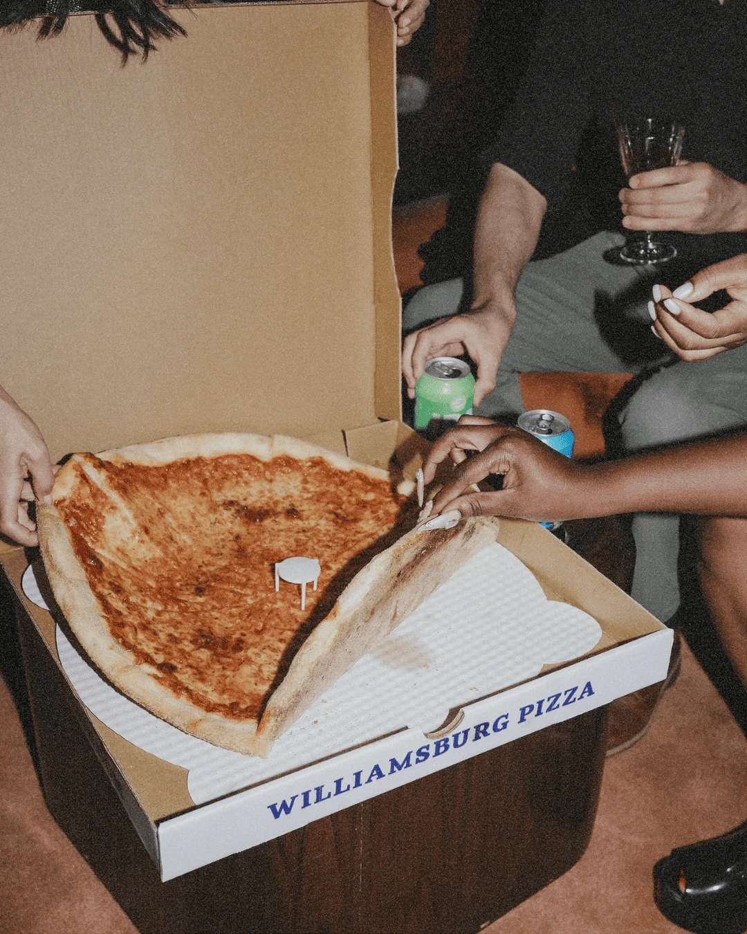 People grabbing pizza from a pizza box