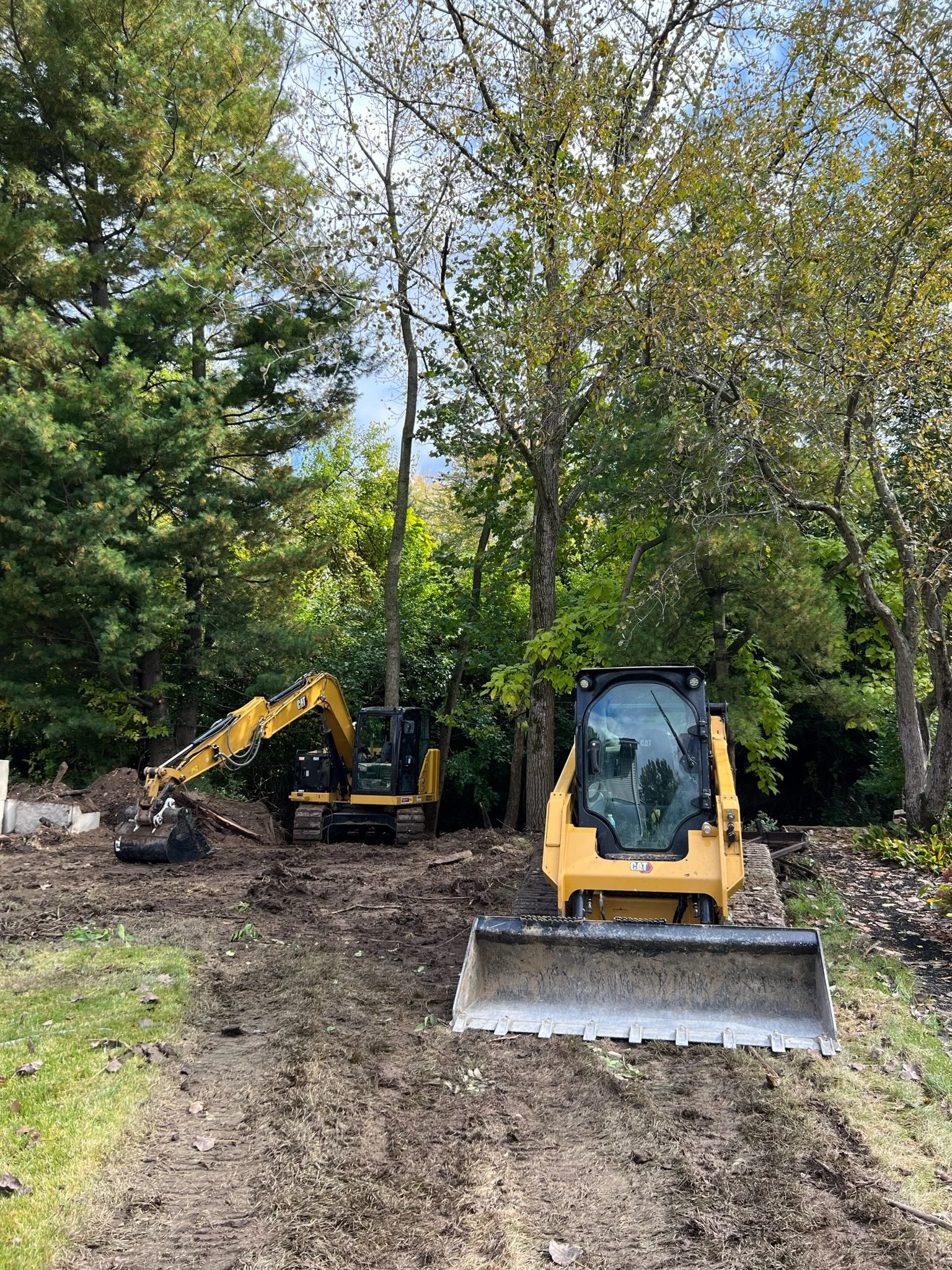 Construction site with two yellow excavators working on dirt clearing among trees.