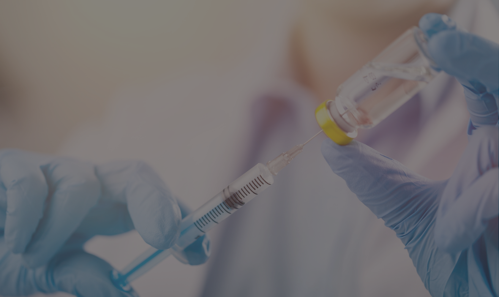A healthcare professional wearing blue gloves drawing liquid from a small vial into a syringe.