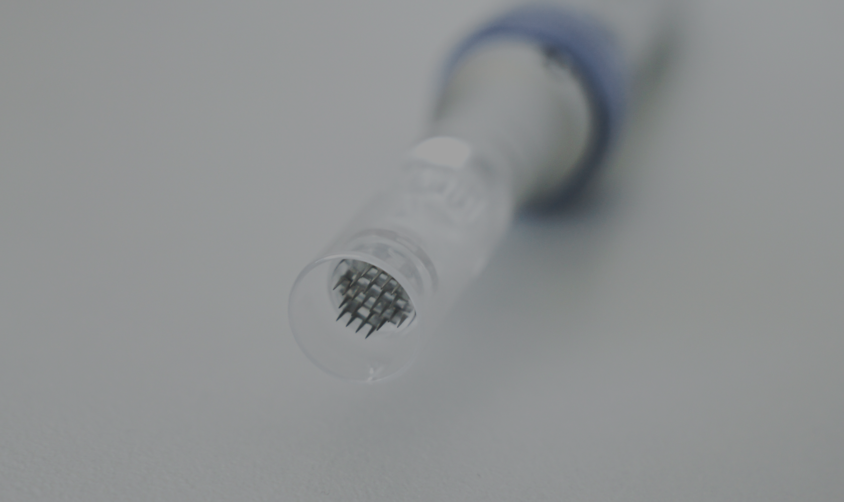 Close-up of a needle point on a medical or dental instrument, with a clear handle and a loop at the end, lying on a white surface.