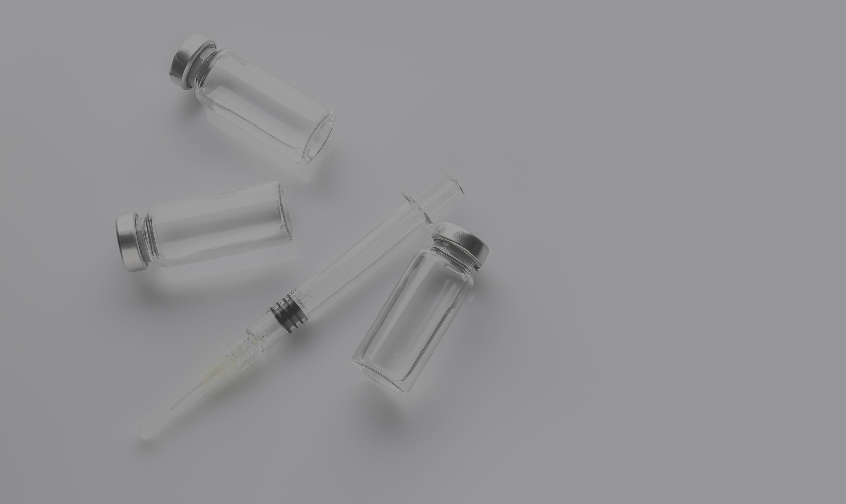 Three small glass vials, a glass syringe, and a glass dropper on a light gray background