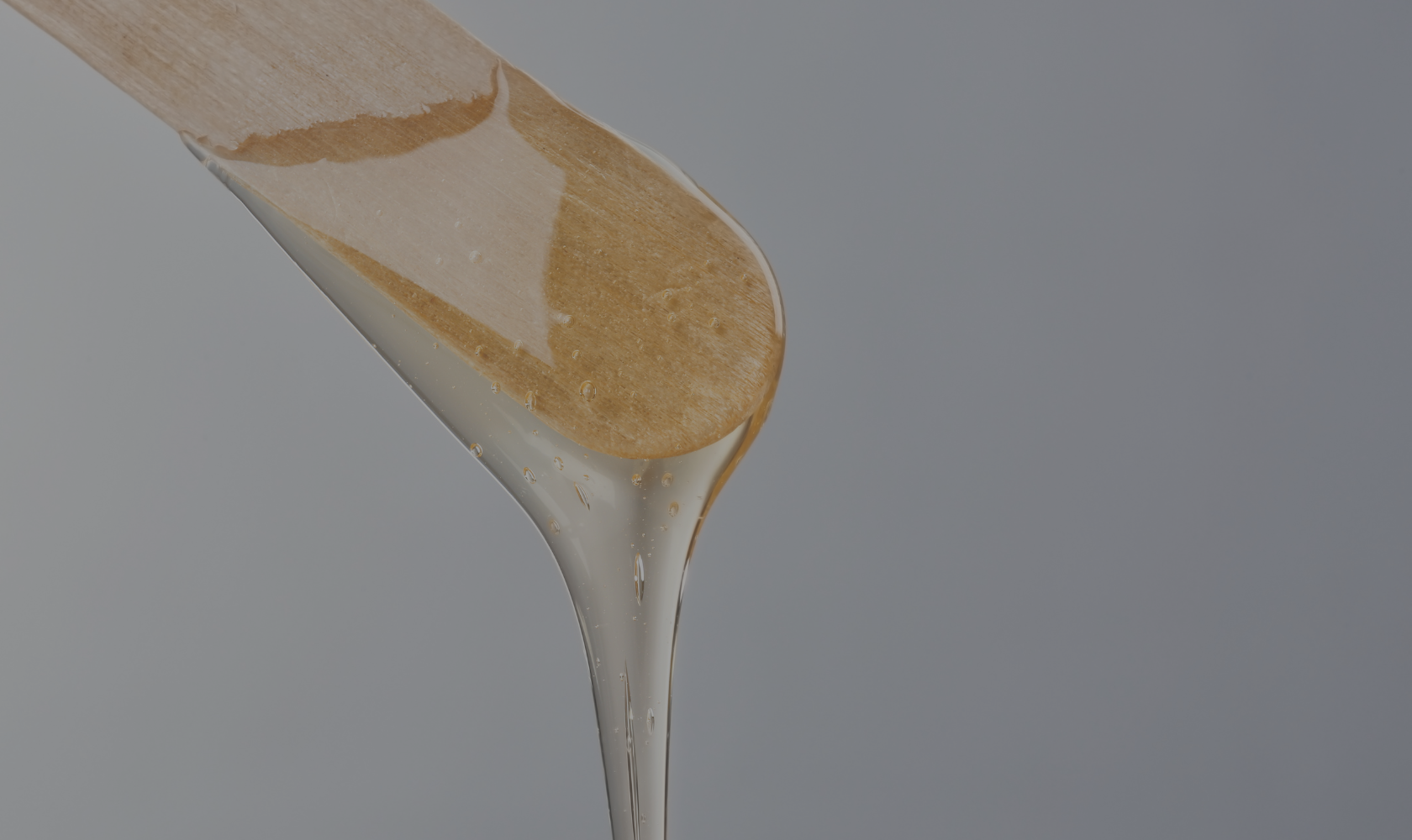 Close-up of honey being poured from a wooden spoon against a gray background.