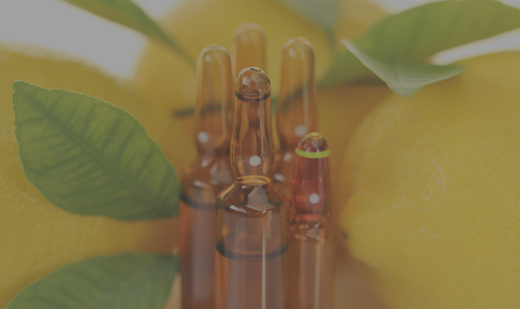 Close-up of several glass ampoules surrounded by green leaves and yellow lemons.