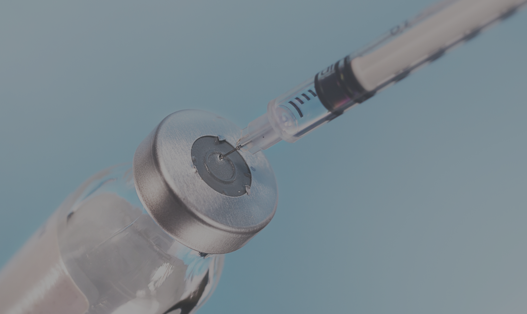 Close-up of a syringe injecting a vaccine into a vial against a light blue background.