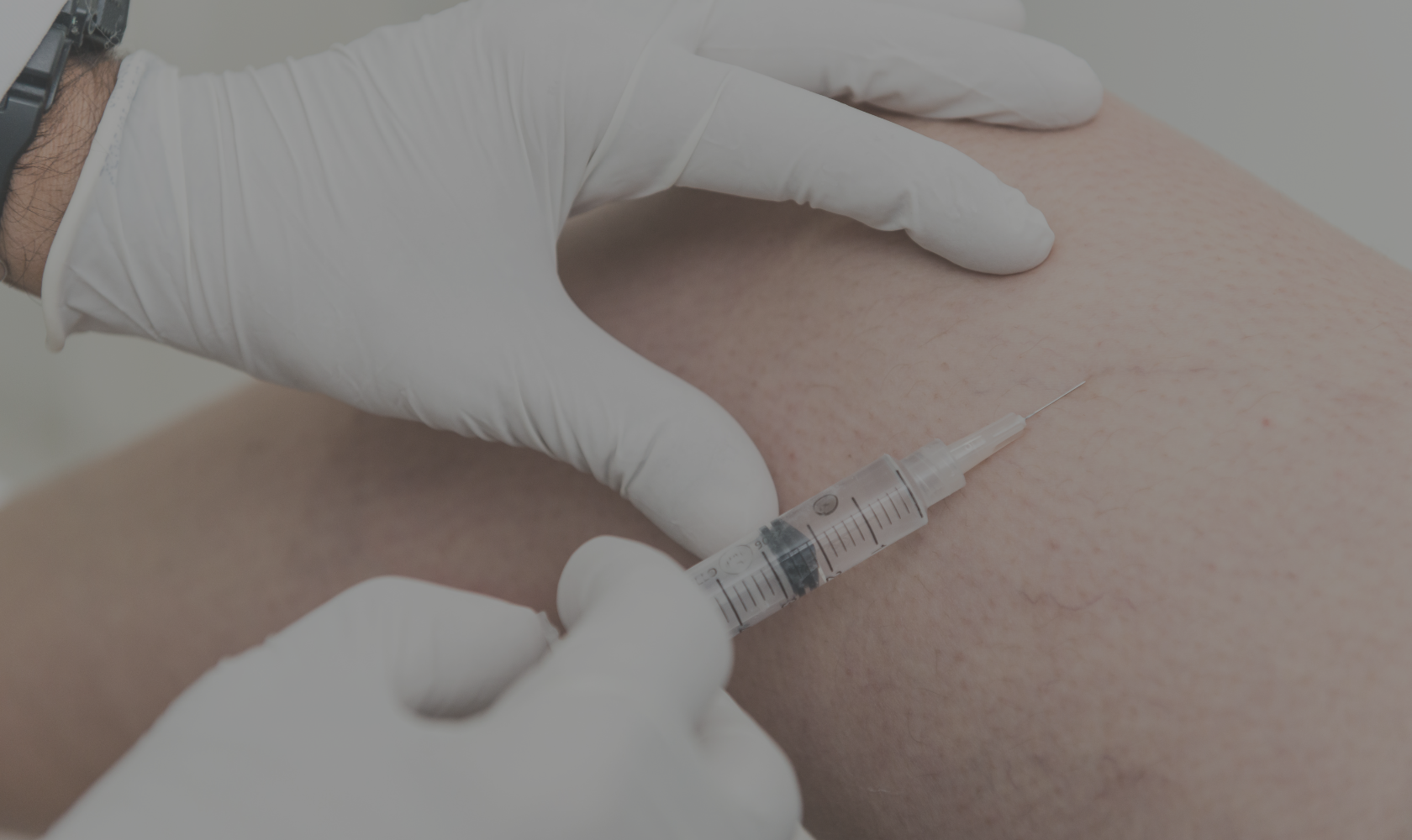A healthcare professional in gloves administering an injection into a patient’s arm with a syringe.