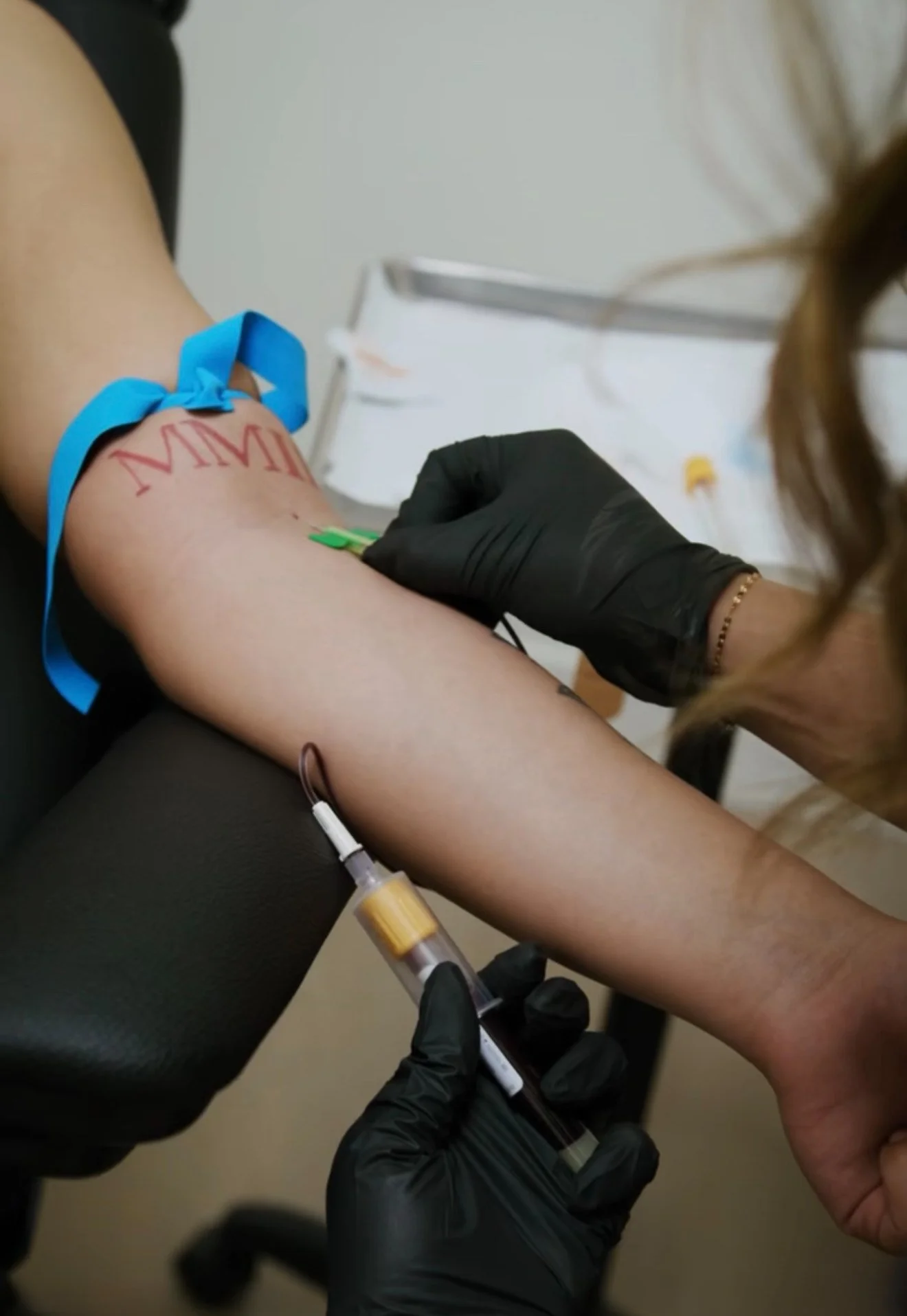 A person receives an injection in their arm, with the word 'MAMI' written on their skin, during a medical procedure.