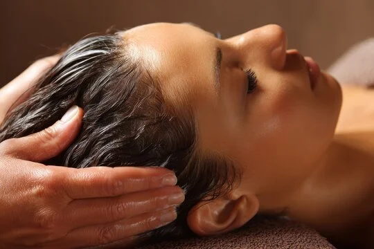 A person receiving a head massage or scalp massage with closed eyes.