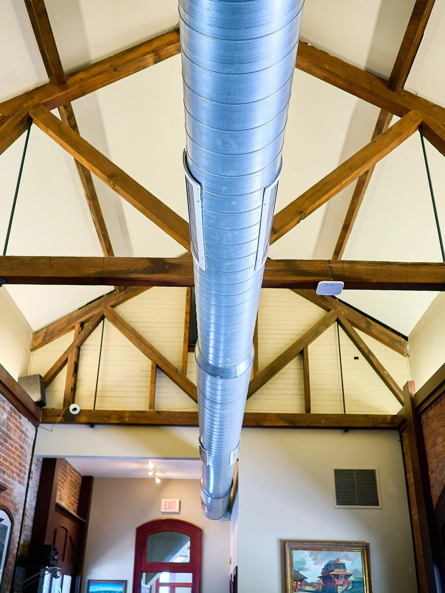 Interior view of a ceiling with exposed wooden beams and a large metal ventilation duct running down the center.