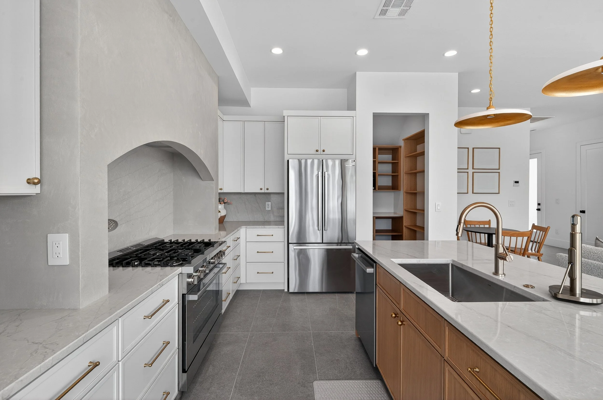 Modern kitchen with white cabinets, a marble countertop island, stainless steel appliances, a double sink, and pendant lighting.