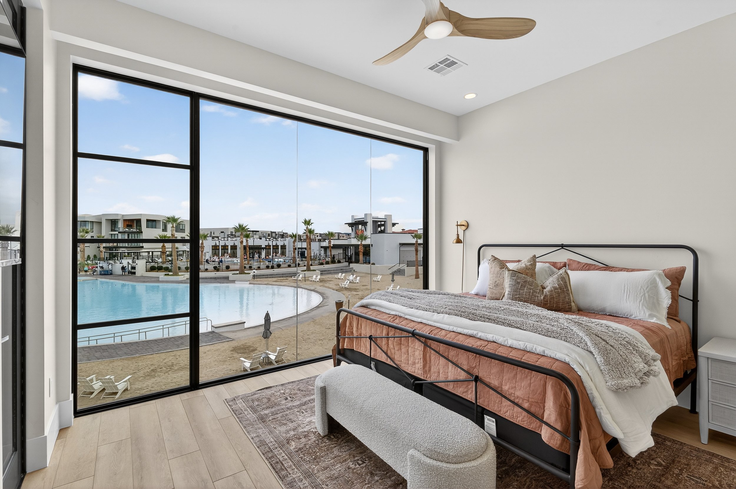Bedroom with large glass window overlooking pool and modern buildings outside