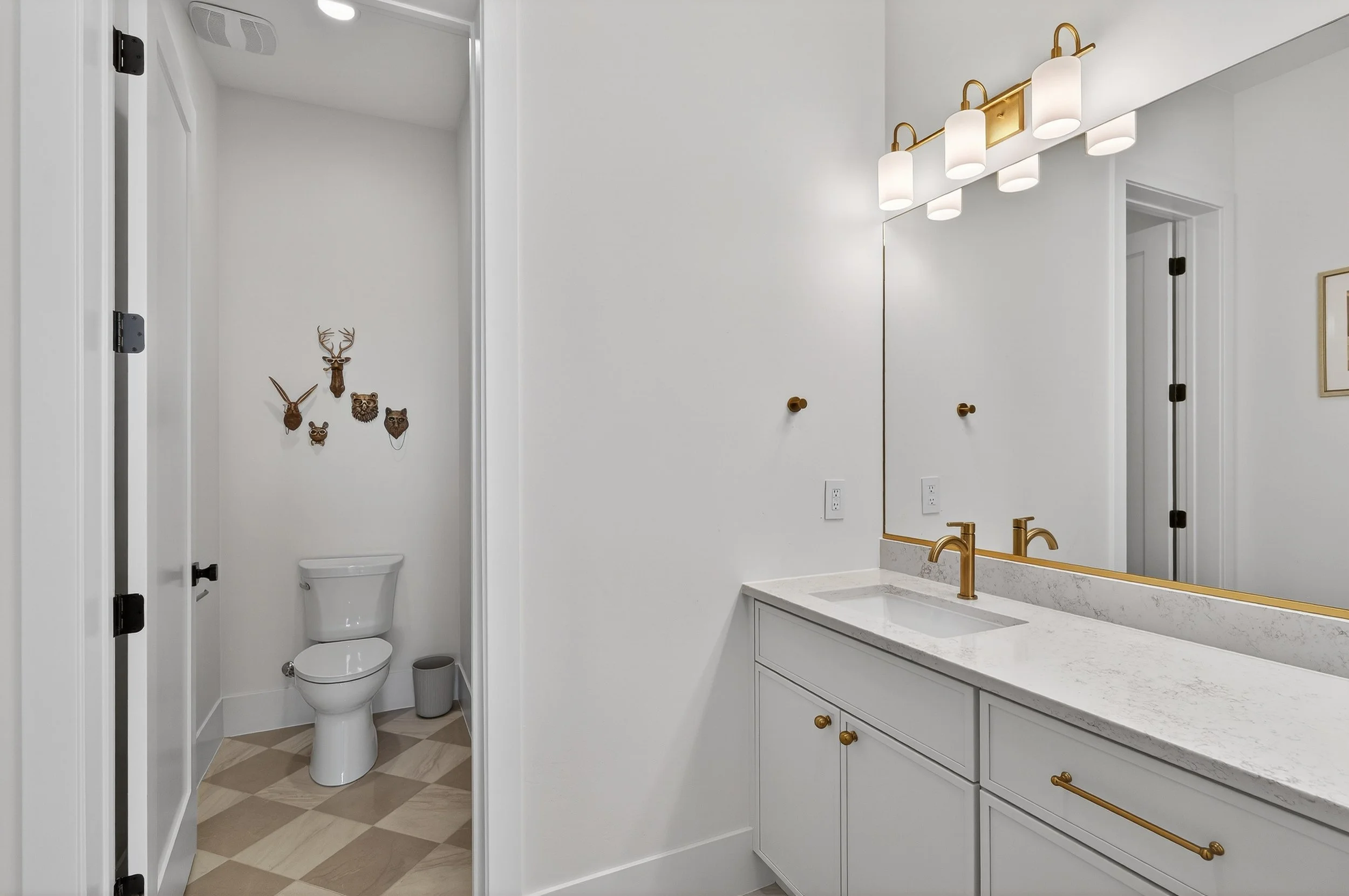 Bathroom with white vanity, gold fixtures, large mirror, and decorative animal and antler wall decor.