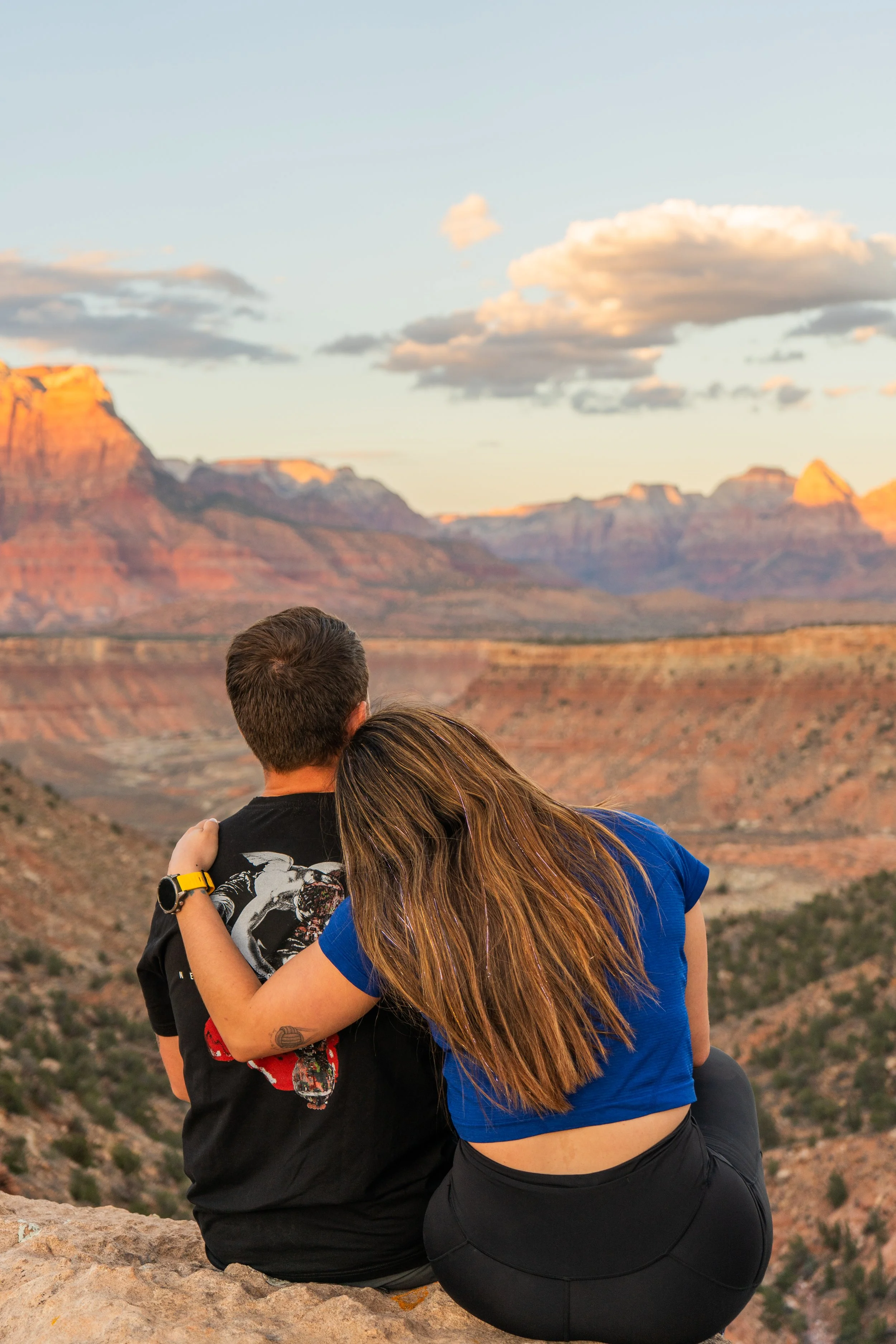 A couple sitting on a rock ledge overlooking the Grand Canyon at sunset.