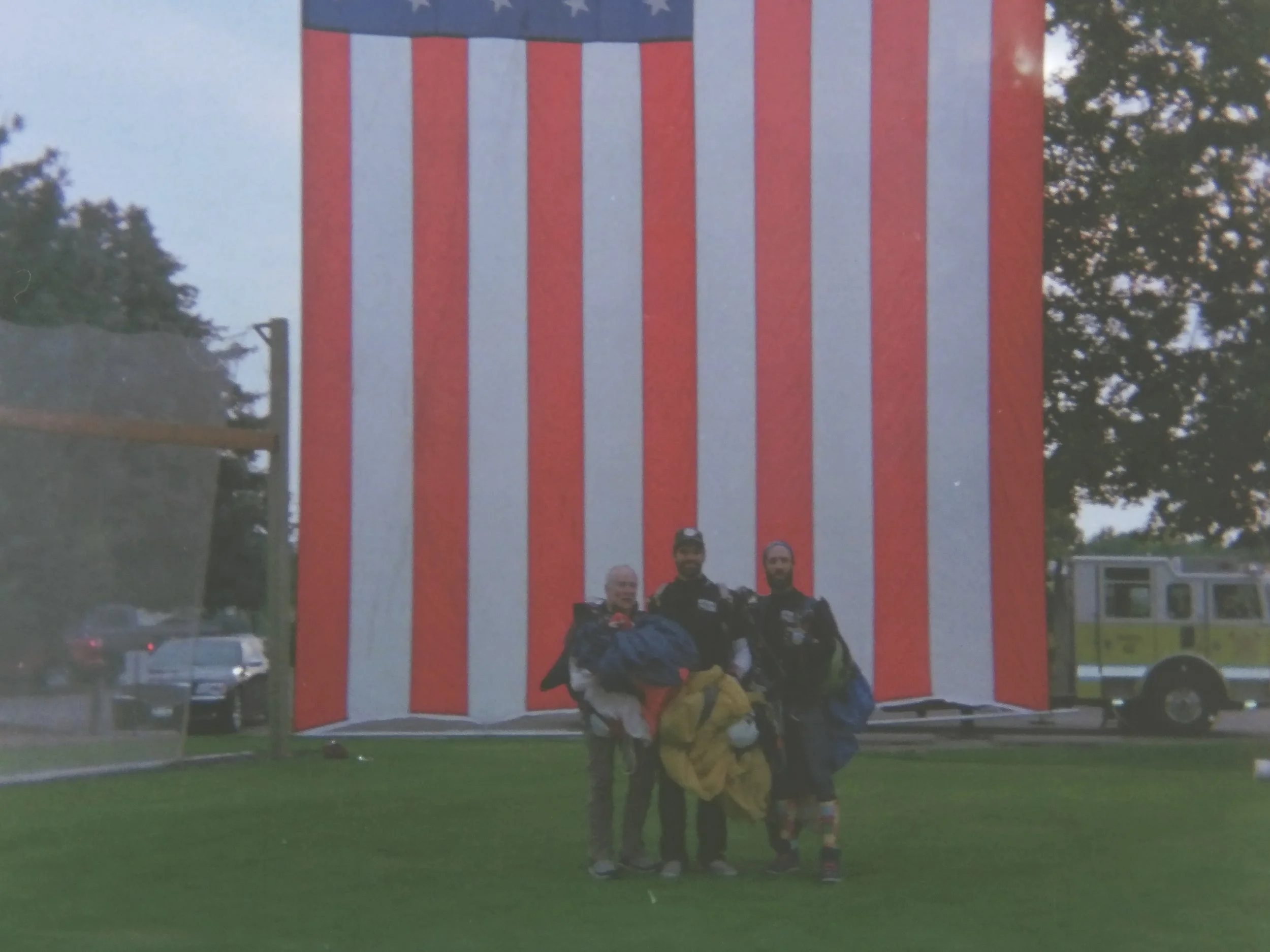 Skydive Skydown team members Rob Herndon, Jordon Basurto, and Mike Sousa at a 9/11 skydiving demo at Eagle Hills Golf Course with the American flag.
