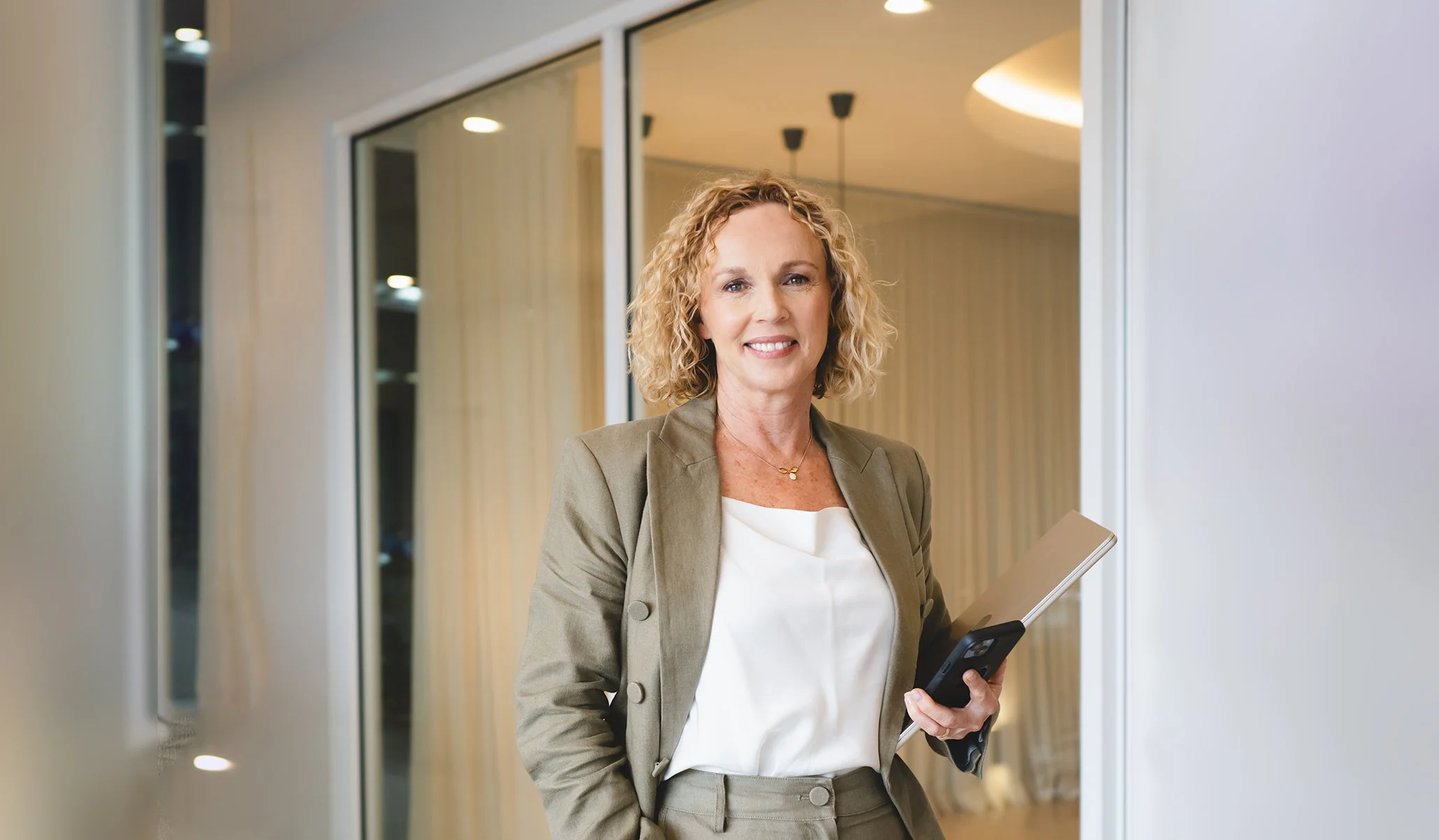 Professional woman in business attire holding a tablet and smiling in an office setting.