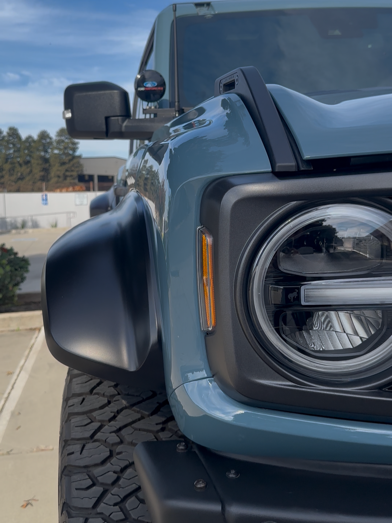Close-up of the front part of a blue off-road vehicle showing the headlight, tire, and side mirror.