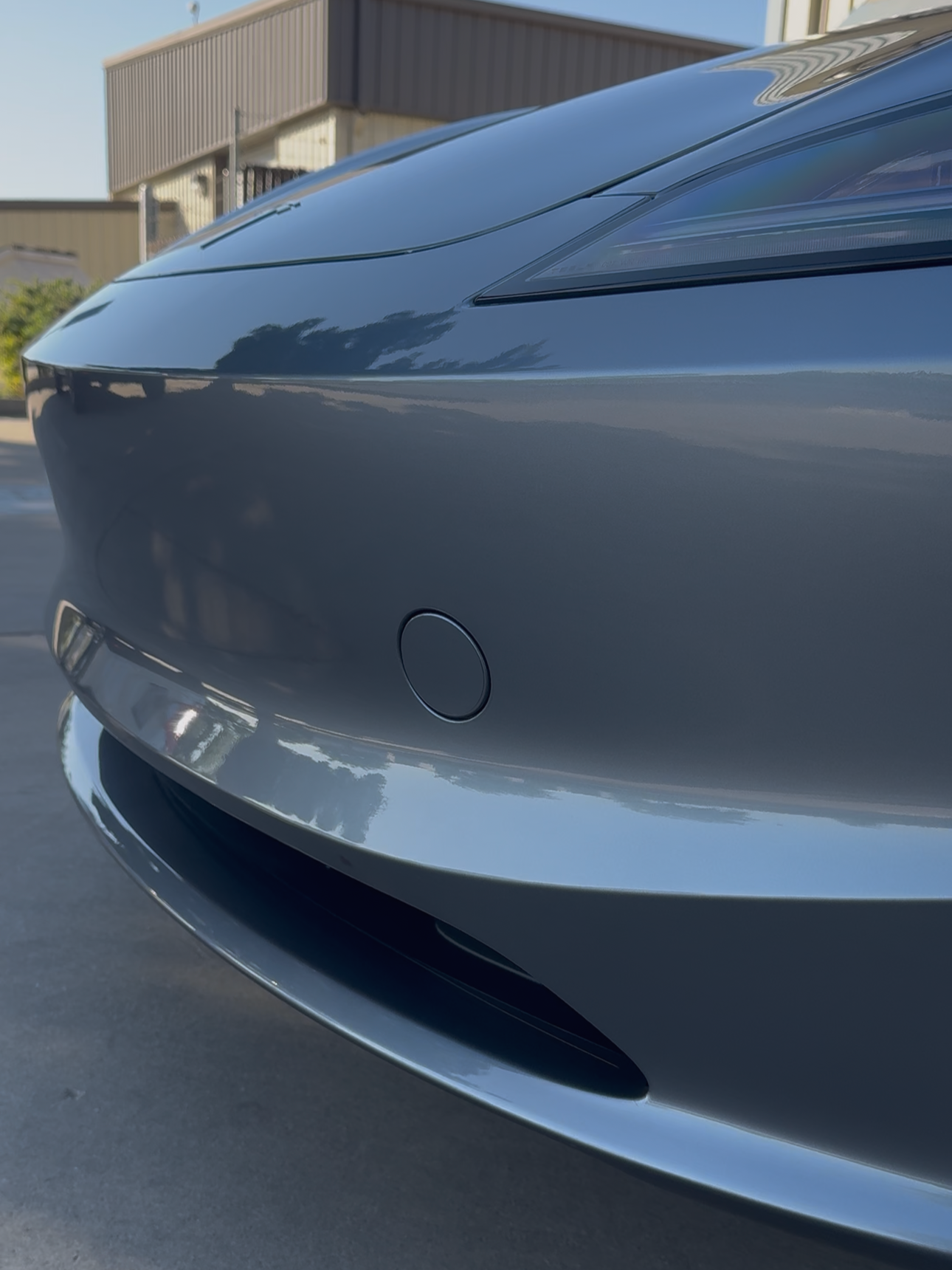 Close-up of the front of a sleek, dark-colored car with modern headlights, parking sensor, and chrome accents on the bumper.
