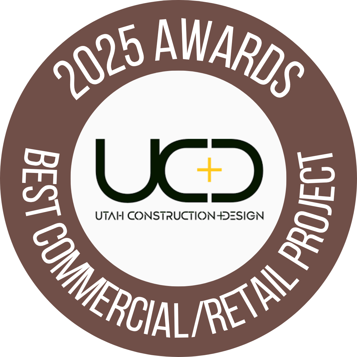 A circular badge with a brown outer ring and white inner circle. The outer ring reads "2025 Awards Best Commercial/Retails Project". The center displays the logo for Utah Construction + Design, with stylized black letters "UCD" and a yellow plus sign above the words "Utah Construction + Design".