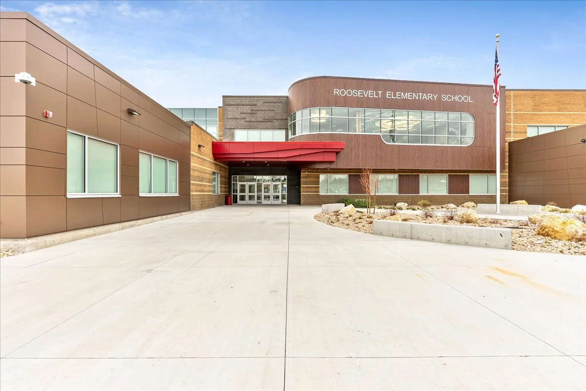 Front view of Roosevelt Elementary School building with a flagpole and American flag in front.