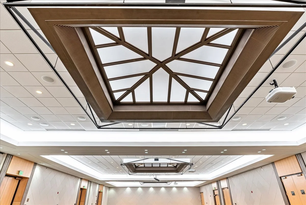 Ceiling with large square decorative light fixture and a projector mounted on the ceiling in a conference room.