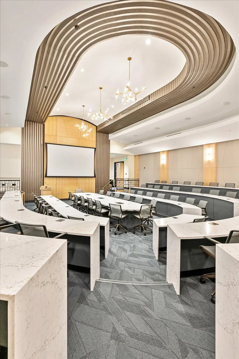 Modern conference room with tiered seating, a large projection screen, and distinctive ceiling chandeliers.