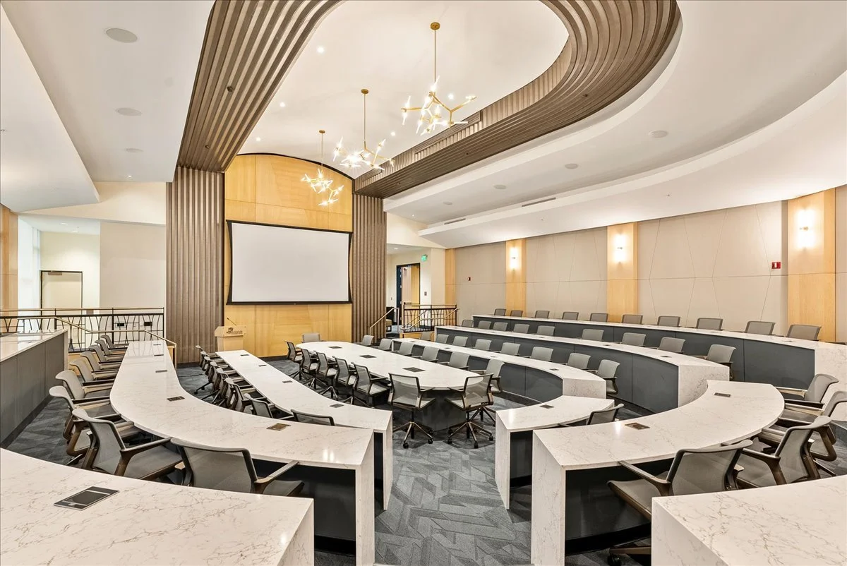 A modern, empty conference room with tiered seating, a large projection screen, and a central table for meetings.