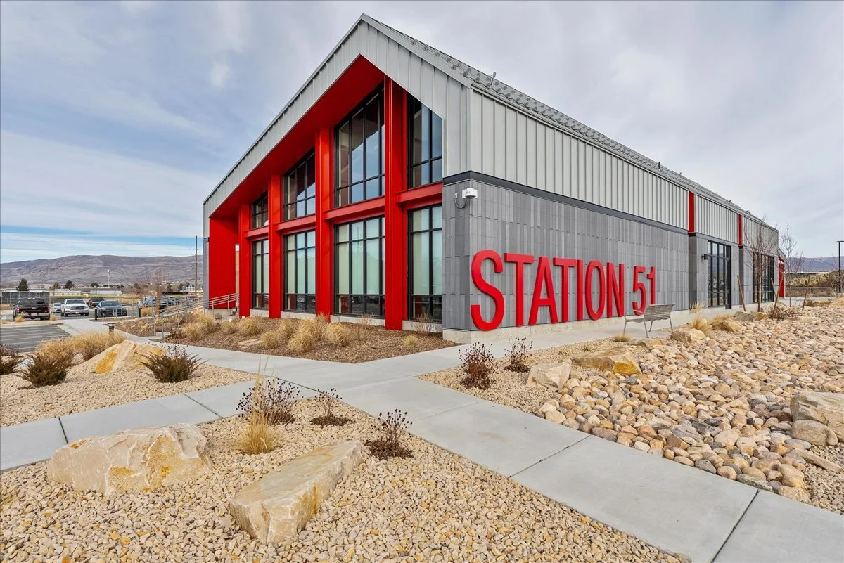 Exterior view of a modern building labeled 'Station 51' with gray and red accents, surrounded by a rocky landscape and parking lot in the background.