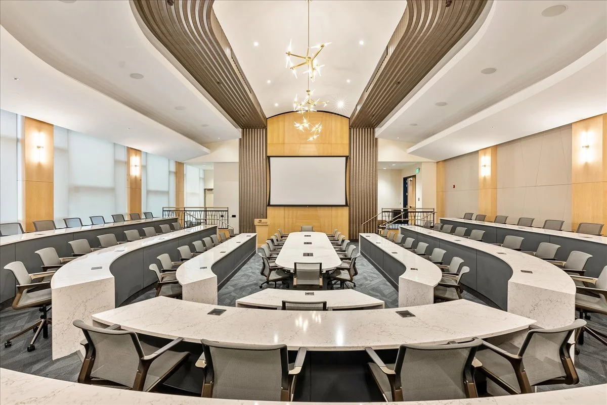 Empty modern conference room with tiered seating and a large screen on the back wall.