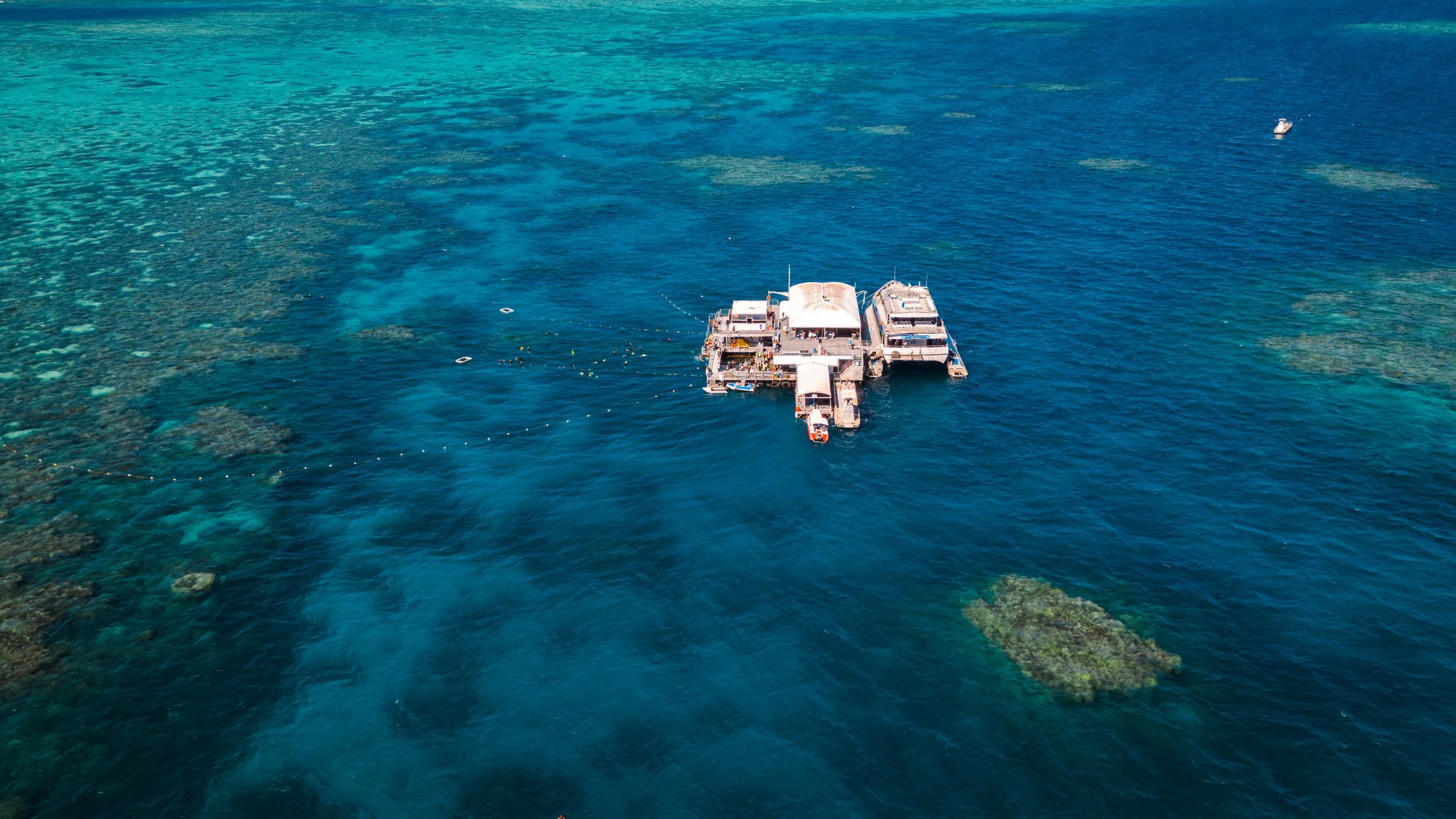 An aerial view of a docked boat in clear blue ocean water with coral reefs visible beneath the surface.
