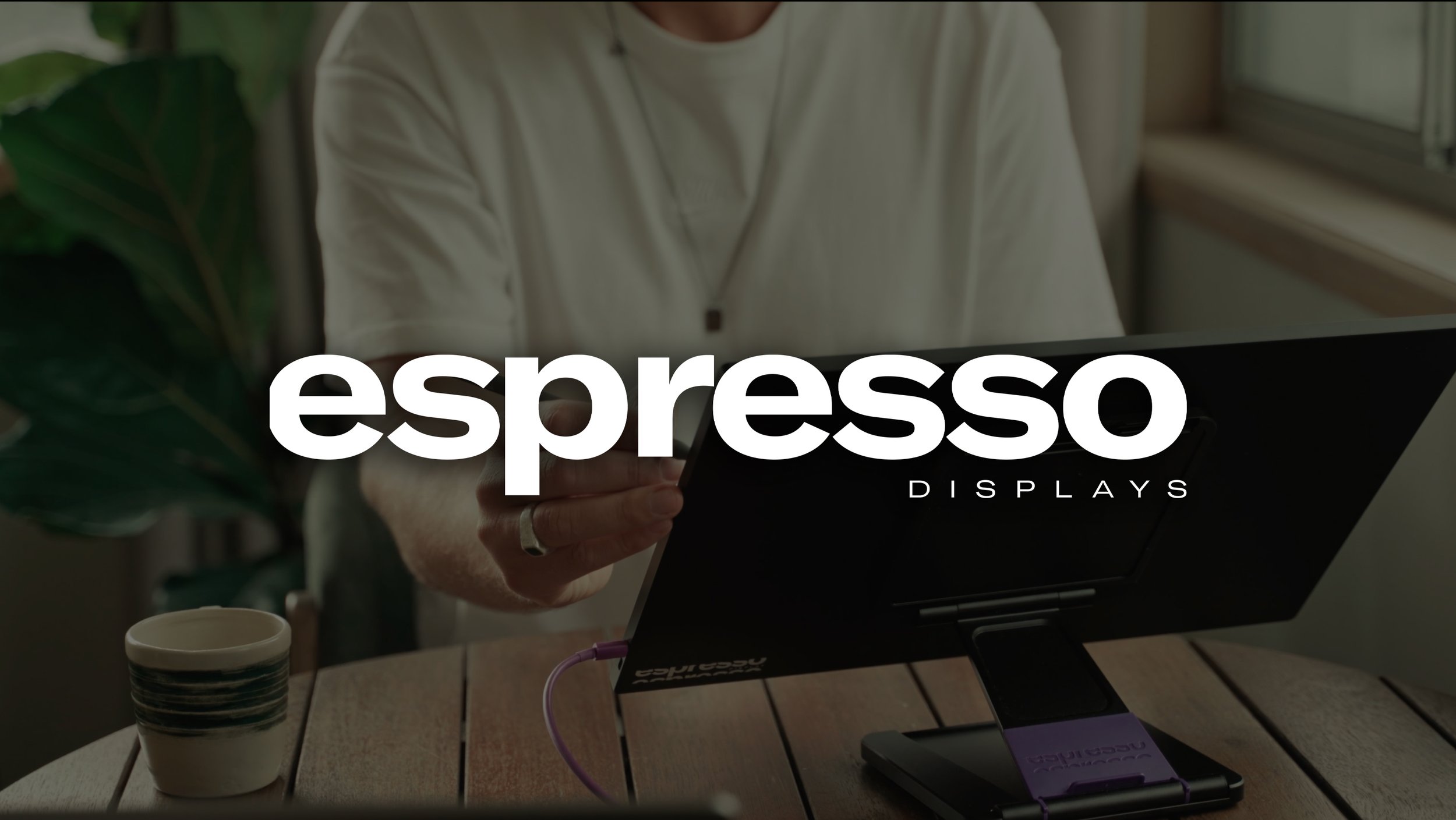 A person working on a laptop at a wooden table with a coffee cup and potted plant nearby, with the words 'espresso displays' overlaid.