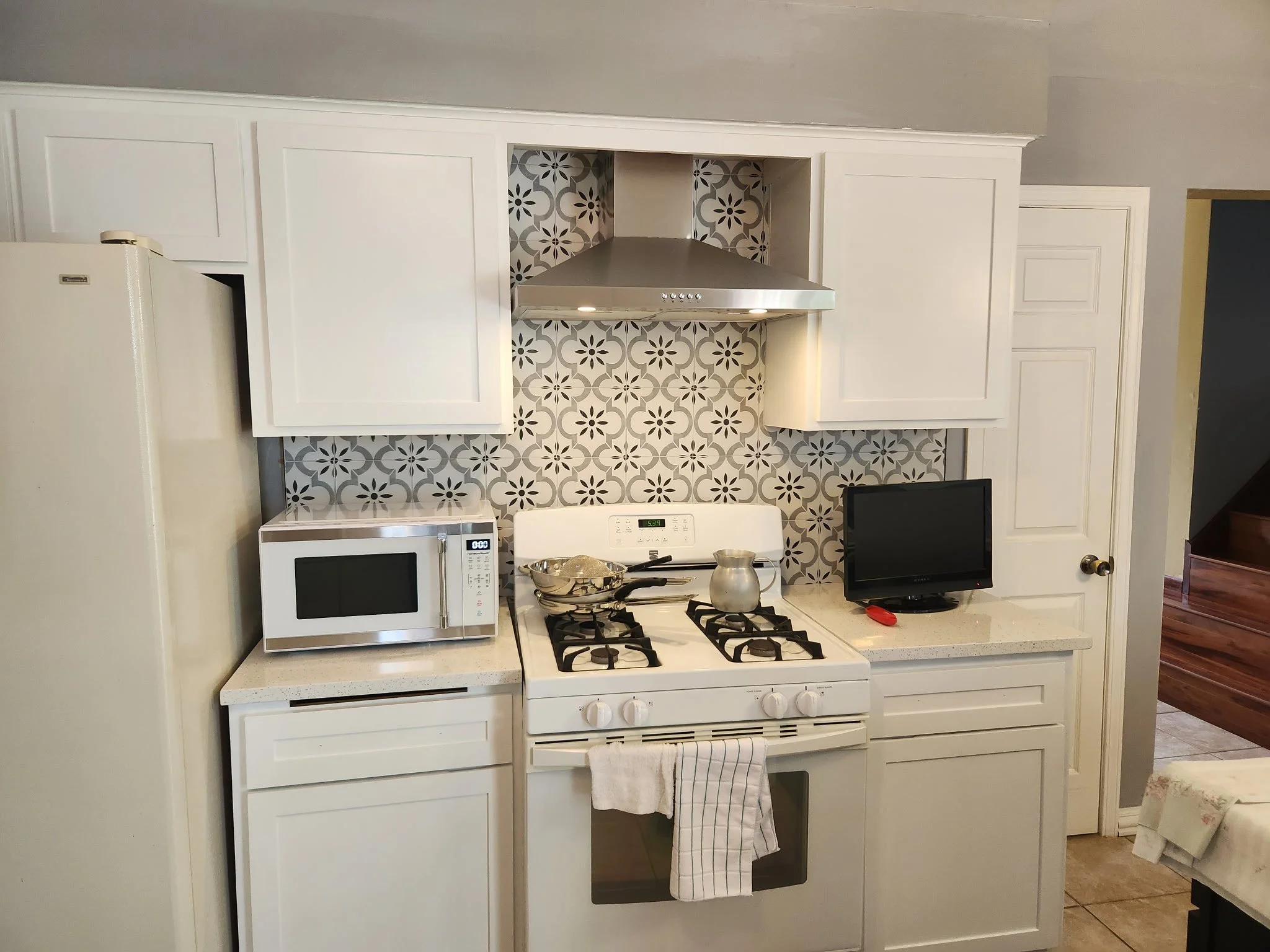 White kitchen with patterned backsplash, microwave, small TV, and cooking utensils on the stove.